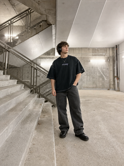 
Model trägt das schwarze Recreate Yourself Tee in einer Beton-Parkgarage