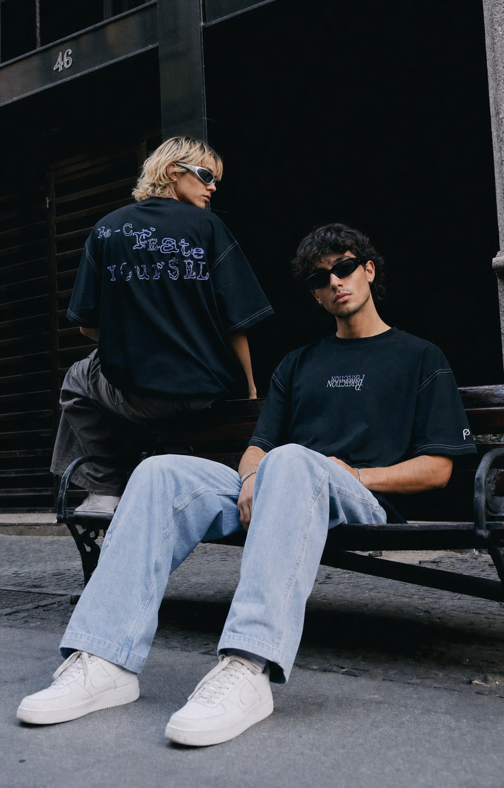 
Zwei Models zeigen Vorder- und Rückseite des schwarzen Recreate Yourself Tees auf einer Parkbank